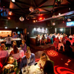 Cette photo montre l'intérieur chaleureux et animé du Knokke Out Zoute, où des convives profitent d'un dîner raffiné, suivi d'une ambiance dansante. Les tables joliment dressées et l'éclairage festif, rehaussé par des boules disco et des projections lumineuses, créent une atmosphère conviviale et chic. Idéal pour des événements d'entreprise ou des soirées privées, cet espace proposé par Tero allie gastronomie et moments de fête dans un cadre sophistiqué et vibrant.