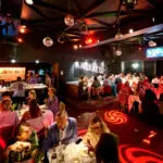 Cette photo montre l'intérieur chaleureux et animé du Knokke Out Zoute, où des convives profitent d'un dîner raffiné, suivi d'une ambiance dansante. Les tables joliment dressées et l'éclairage festif, rehaussé par des boules disco et des projections lumineuses, créent une atmosphère conviviale et chic. Idéal pour des événements d'entreprise ou des soirées privées, cet espace proposé par Tero allie gastronomie et moments de fête dans un cadre sophistiqué et vibrant.