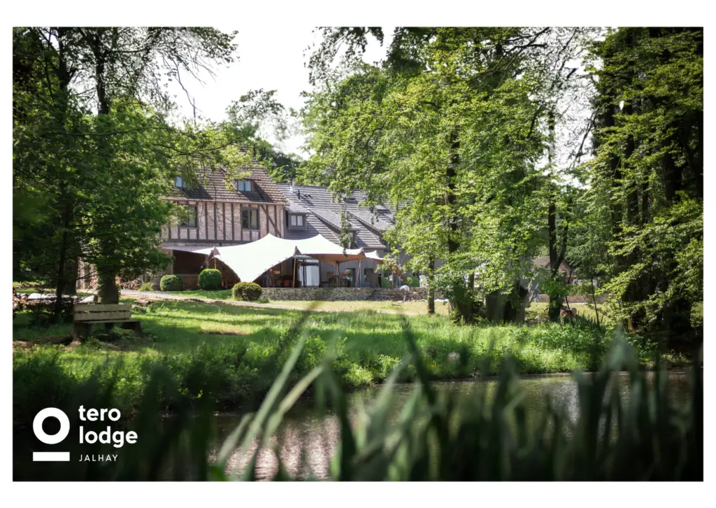 Cette carte postale de tero capture toute la beauté et l’authenticité du Tero Lodge Jalhay, un lieu d’exception niché au cœur de la nature. Entouré d’une forêt verdoyante et bordé par un étang paisible, ce magnifique bâtiment à colombages incarne le charme et l’élégance d’un refuge en pleine campagne. Une grande tente beige, installée en terrasse, offre un espace de détente et de convivialité pour profiter du cadre enchanteur. Loin du tumulte urbain, Tero Lodge invite à un séjour ressourçant, où gastronomie, bien-être et nature s’unissent pour une expérience inoubliable.