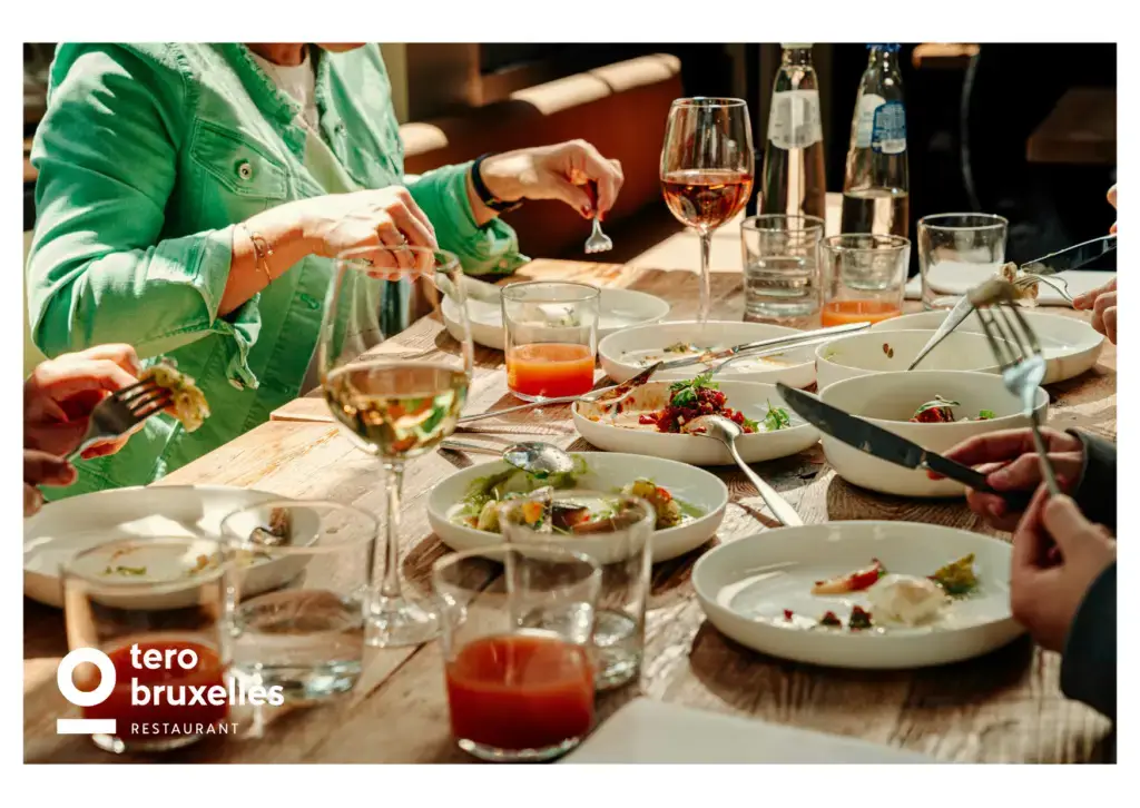 Cette carte postale illustre l’ambiance chaleureuse et conviviale du restaurant Tero Bruxelles, où gastronomie rime avec partage. Autour d’une grande table en bois, plusieurs convives dégustent un repas composé de plats savoureux et colorés, présentés dans des assiettes blanches élégantes. Les verres de vin blanc et de rosé, ainsi que les jus frais, viennent compléter cette expérience culinaire authentique. La lumière naturelle illumine la scène, accentuant la simplicité et l’élégance de l’instant. Tero Bruxelles incarne une cuisine locale et responsable, privilégiant des produits frais et de saison, dans un cadre propice aux échanges et aux plaisirs gourmands.